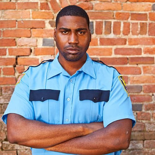 Afroamerican security guard in front of old brick wall.